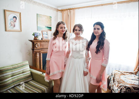 Fabelhafte junge Braut mit zwei wunderschönen Brautjungfern in rosa Kleider in hellen Zimmer posieren. Stockfoto