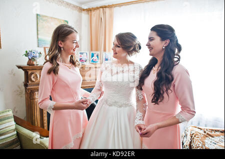 Fabelhafte junge Braut mit zwei wunderschönen Brautjungfern in rosa Kleider in hellen Zimmer posieren. Stockfoto