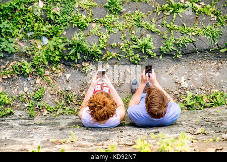 Junges Paar mit Smartphones in der Stadt, liest oder schaut etwas an. Sonniger Frühlingstag. Hochwinkelansicht. Stockfoto
