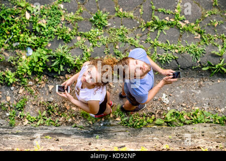 Schöne junge Paar mit Smart Phones in der Stadt, bis suchen. sonniger Frühlingstag. hohe Blickwinkel betrachten. Stockfoto