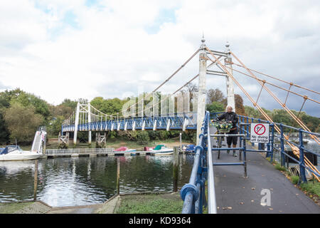 Ein Radfahrer steigt aus und geht über Teddington Lock Footbridge auf der Themse, Teddington, England, Großbritannien Stockfoto