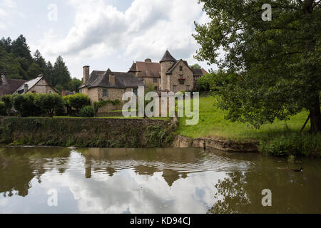 SEGUR-LE-CHATEAU, Frankreich - 30. JUNI 2017: Blick über den Fluss Auvezere, mit ein paar Enten, zu einem malerischen mittelalterlichen Teil des Dorfes in der Stockfoto