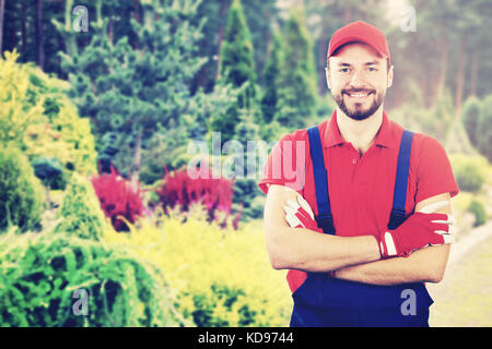Junge lächelnde Gärtner mit verschränkten Armen im Garten stehen Stockfoto