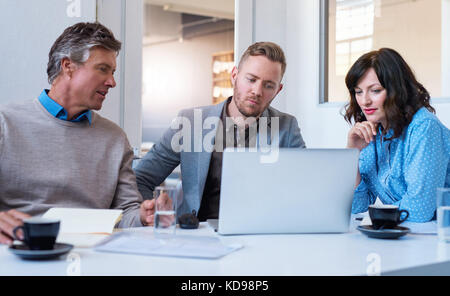 Drei fokussierte Geschäftsleute mit einem Laptop zusammen in einem Büro Stockfoto