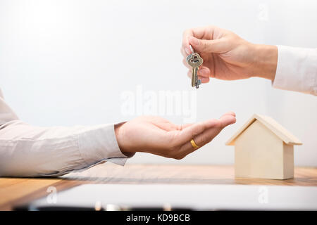 Immobilienmakler in Anzug in einem Büro Schreibtisch Übergabe der Hausschlüssel mit Kunden nach Vertragsunterzeichnung sitzen. Stockfoto