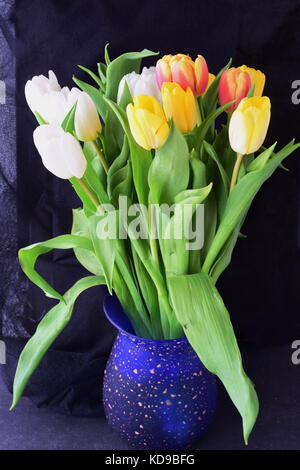 Blumenstrauß aus den vielfarbigen Tulpen in einer blauen Vase auf einem grauen Tuch. Frühling Blumen. Romanze Stockfoto