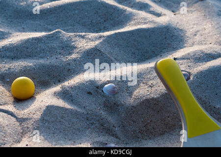 Paddel und gelbe Kugel auf einem Sandstrand Stockfoto