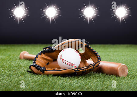 Baseball-Handschuh mit Baseball und Bat liegend auf dem grünen Rasen Stockfoto