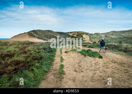 Hundespaziergängen in der Holywell Bay - ein Mann, der seinen Hund durch die Dünen der Holywell Bay in Cornwall spaziert. Stockfoto