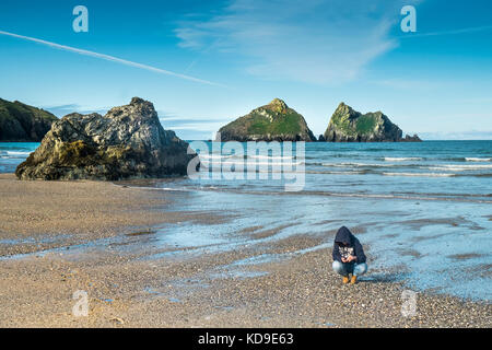 Eine Frau, die Muscheln am Holywell Bay Strand untersucht. Gull Rocks an der Holywell Bay einer der kultigen Poldark-Drehorte in Cornwall. Stockfoto