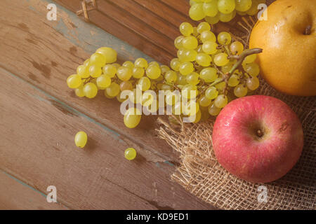 Rote Äpfel und Trauben auf Bambus tablett mit Tuch Säcke auf dem Holz. Stockfoto