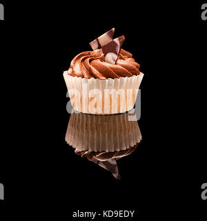 Ein muffin Cupcake mit braun Creme und Stücke Schokolade in einem Pappbecher. Auf einem schwarz glänzenden Hintergrund mit echten Reflexion. isoliert auf Schwarz Stockfoto
