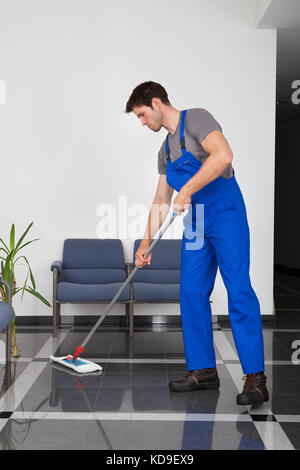 Portrait des jungen Mannes, den Boden mit Mop im Büro Stockfoto