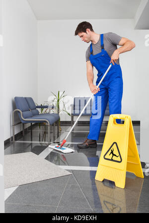 Portrait des jungen Mannes, den Boden mit Mop im Büro Stockfoto