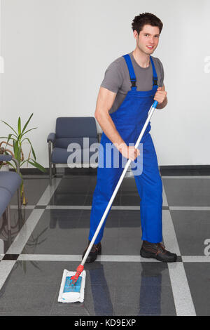 Portrait des jungen Mannes, den Boden mit Mop im Büro Stockfoto