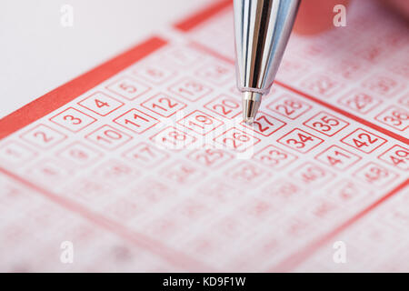 Nahaufnahme einer Person Nummer auf Lottoschein mit Stift markieren Stockfoto