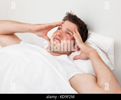 Junge Menschen leiden unter Kopfschmerzen liegend auf Bett Stockfoto