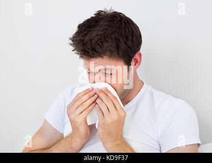 Junger Mann bläst seine Nase In einem weißen Papiertuch Stockfoto