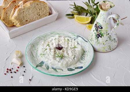 Hausgemachte griechische traditionelle Sauce Tzatziki mit Gurke, Knoblauch, Joghurt und Zitronensaft in eine Schüssel geben und Glas mit Olivenöl auf einen abstrakten Hintergrund. Gesunde e Stockfoto