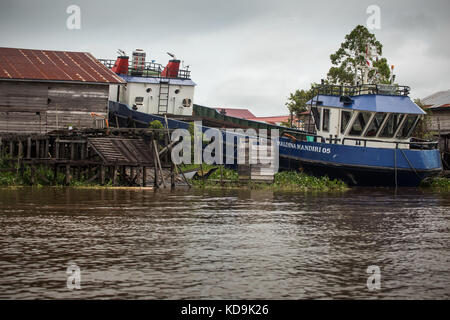 Einzigartige borneo Boote angedockt an Land am Ufer des Flusses Mahakam und. Blick vom Fluss am Land mit Holz- Dritte Welt shack Struktur Stockfoto