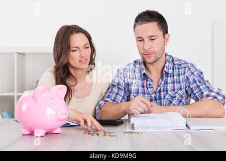 Junger Mann, Blick auf Frau einfügen Münze im Sparschwein Stockfoto