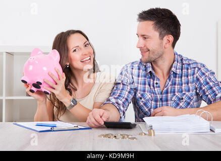 Junger Mann, Blick auf Frau einfügen Münze im Sparschwein Stockfoto