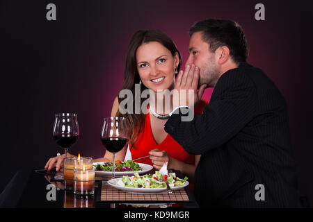 Mann am Esstisch Weibes Ohr zu flüstern Stockfoto