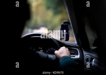 Ein kaukasischer Mann, dessen Gesicht verdunkelt ist ein Uber fährt Taxi, und hat das Firmenlogo auf seinem Smartphone, die an der Windschutzscheibe befestigt ist. Stockfoto