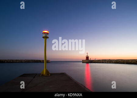 Marine eines kleinen Leuchtturm mit seinem roten Reflexionen über das Meer bei Sonnenuntergang. Einige Leute sind die Fischerei unter dem Sternenhimmel. Foto bei Sonnenuntergang in S Stockfoto