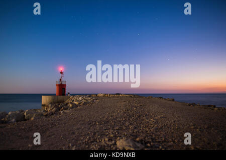 Marine eines herzhaften Straße, die zu einem kleinen beleuchteten Leuchtturm führt. Foto bei Sonnenuntergang in Sabaudia, Italien. Stockfoto