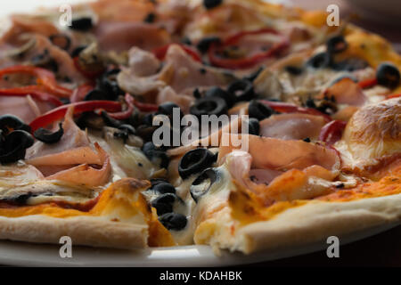 Pizza mit Schinken, Käse, in Scheiben geschnittene Oliven, Salami und Pilzen Nahaufnahme Seitenansicht Stockfoto