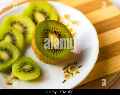 In Scheiben geschnittene Kiwis auf einer weißen Platte, Holzbrett, Ansicht von oben Stockfoto