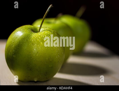 Drei Äpfel in einer diagonalen Linie auf einer hölzernen Oberfläche mit dunklen Hintergrund angeordnet Stockfoto