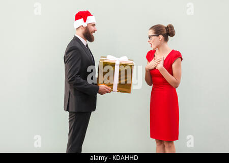 Der bärtige Mann in Rot Schale ein Geschenk geben schöne Frau. Studio shot auf grauem Hintergrund Stockfoto