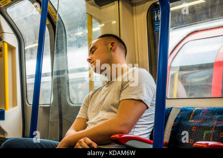 Londoner U-Bahn - junger Mann schläft, das Tragen von Kopfhörern An einem ruhigen Tag Reise ohne andere Passagiere in den Schlitten ein. England, UK. Stockfoto