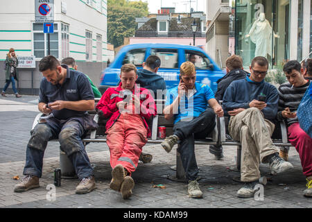 Junge Männer Bauarbeiter, Tragen von Arbeitskleidung, eine Pause machen und draußen auf einer Bank sitzen, in South Kensington, London, England, UK. Stockfoto
