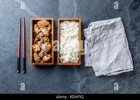 Japanisches Essen. Chicken Teriyaki mit Reis in Holz- Bento Lunch Box. Schiefer Hintergrund, Ansicht von oben Stockfoto