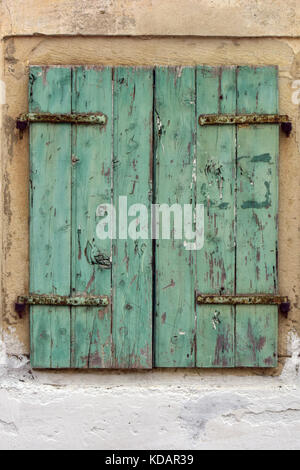 Ein paar grün gestrichenen Fensterläden, die ein Fenster in einem alten Bauernhaus mit abblätternde Farbe und einer beunruhigten rustikalen Stil in shabby chic Designs. Stockfoto