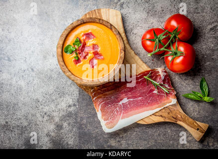 Spanische Tomatensuppe Salmorejo serviert in Olivenöl hölzerne Schüssel mit Schinken Jamón Serrano auf Stein Hintergrund. Ansicht von oben, kopieren. Stockfoto