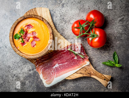 Spanische Tomatensuppe Salmorejo serviert in Olivenöl hölzerne Schüssel mit Schinken Jamón Serrano auf Stein Hintergrund. Ansicht von oben. Stockfoto