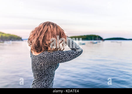 Junge Frau mit den Händen am Kopf unter Haar mit Blick auf die Bucht von Bar Harbor, Maine Stockfoto