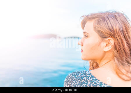 Profil Portrait von Jungen glücklich lächelnde Frau am Rande von Dock in Bar Harbor, Maine sitzen bei Sonnenuntergang mit goldenes Sonnenlicht und tan zu Seite Stockfoto