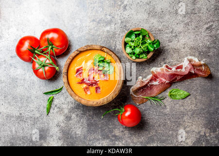 Spanische Tomatensuppe Salmorejo serviert in Olivenöl hölzerne Schüssel mit Schinken Jamón Serrano auf Stein Hintergrund. Ansicht von oben. Stockfoto