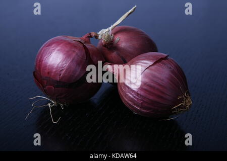 drei rote Zwiebel auf schwarzem Tisch Stockfoto