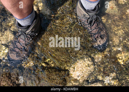 Männliche Wanderer das Waten im seichten Wasser und veranschaulicht den Wert der wasserdichte Wanderschuhe Stockfoto