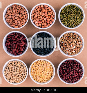 Gemischte Bohnen und Linsen in die weiße Schüssel auf braunem Hintergrund. mung Bean, Erdnuß, Soja, rote Kidney-bohnen, Schwarze Bohne, rote Bohnen, grüne Bohne, mille Stockfoto
