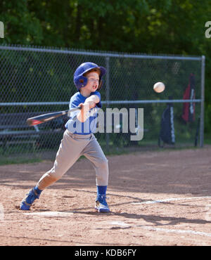 Junge schlagen der Ball beim Spielen Baseball in einem blauen Uniform Stockfoto