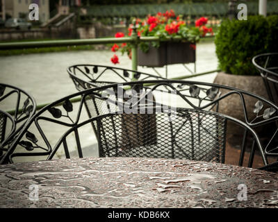 Nahaufnahme eines nassen Coffee house Tabelle im Regen vor einem Fluss und rote Blumen Stockfoto