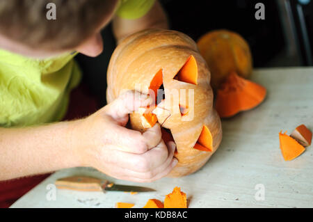 Halloween Kürbis schneiden Prozess, Prozess, Jack-o-Lantern. männliche Hände mit Messer, Reste der Kürbis auf dem Küchentisch. selektive Fokus Stockfoto