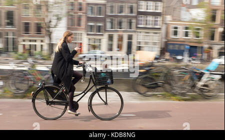 Eine junge Frau überprüft Ihr Telefon als Sie Zyklen durch Amsterdam Stockfoto